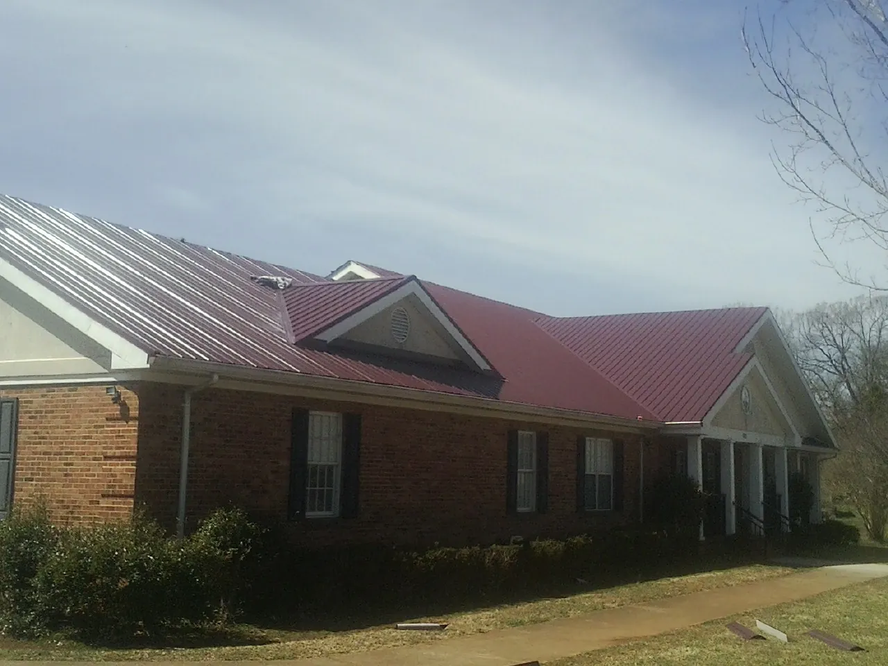 Red metal roof with gabled entries on a long brick building, from a Hail Damage Roof Repair job in Raymond
