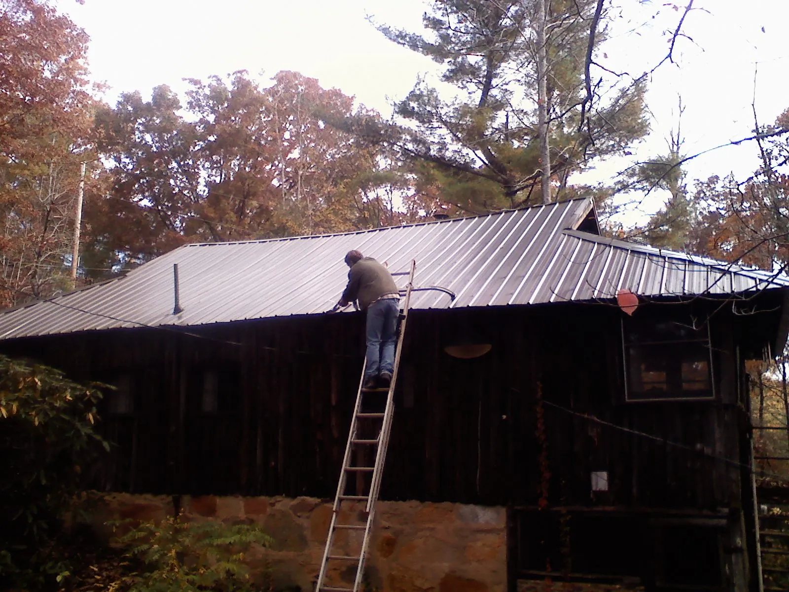 Roofer on a ladder working along the edge of a cabin metal roof in Raymond