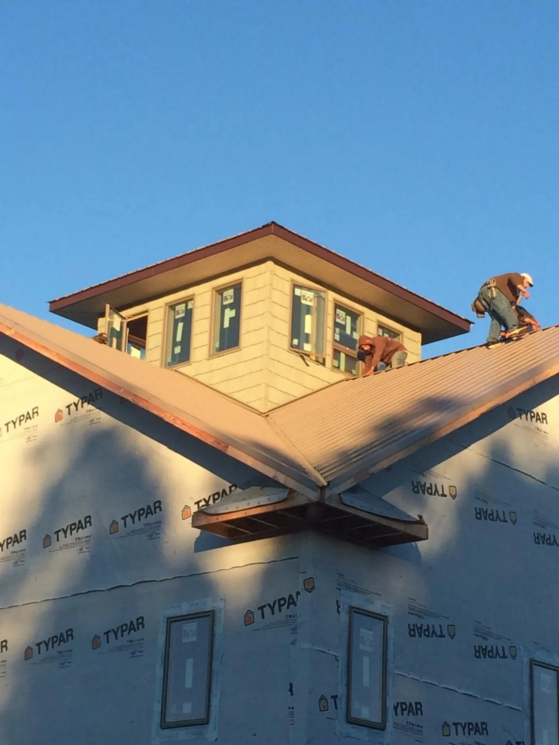 Roofers working around a rooftop cupola on a new metal roof at sunset — Roof Waterproofing in Raymond by Roofing Brothers